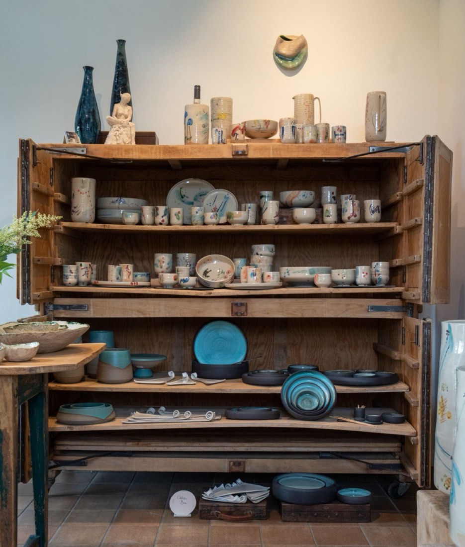 Handmade ceramics displayed in a wooden cabinet in the shop